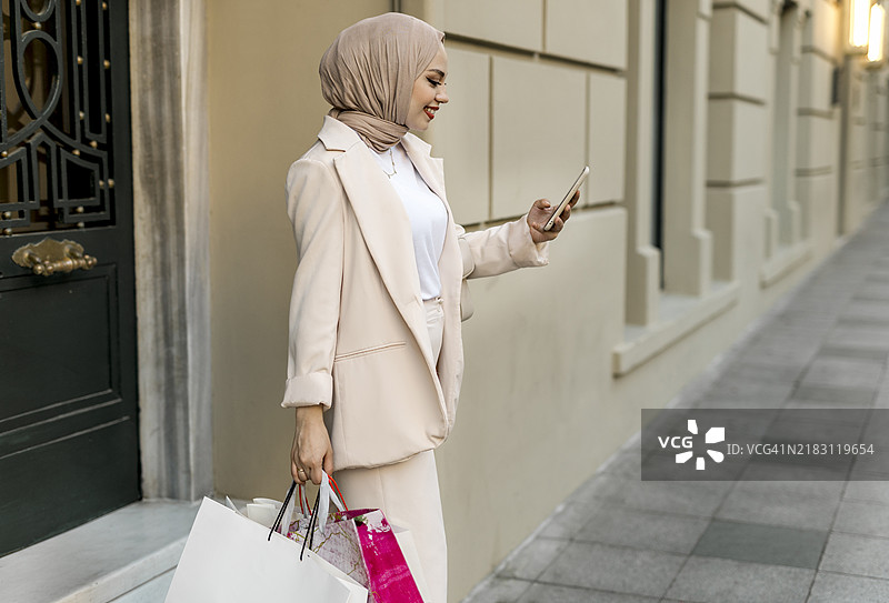 侧面视图的女商人在购物狂欢中，微笑着查看手机上的短信，走在人行道上。图片素材
