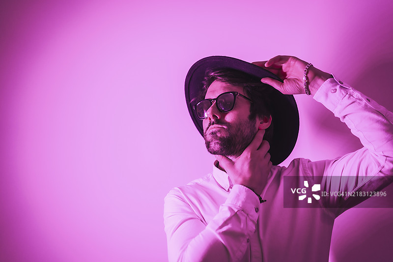 工作室生活方式，一位年轻的白人男性，带着诱人的目光，佩戴着太阳镜，周围有霓虹粉色的灯光，留有复制和粘贴的空间。图片素材