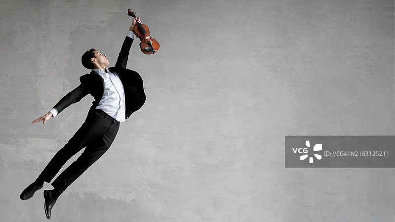 侧面视角的男性音乐家在空中摆姿势，手持小提琴图片素材