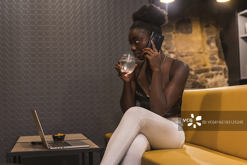 侧面视角的非洲年轻女性在酒吧远程工作时喝水图片素材