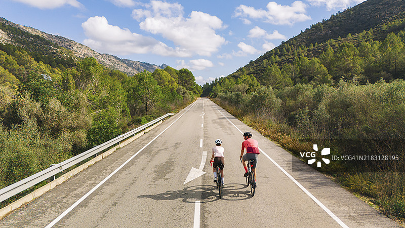 西班牙山区一位成熟男性与他的青少年女儿骑自行车的高空/无人机后视图图片素材