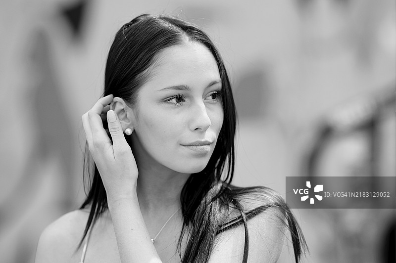 黑白肖像，一位非常年轻的漂亮女性，背景模糊。她用右手将长发拨到耳后。图片素材