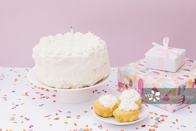 生日蛋糕松饼、礼品盒和五彩纸屑，白色桌子背景下的粉色背景图片素材