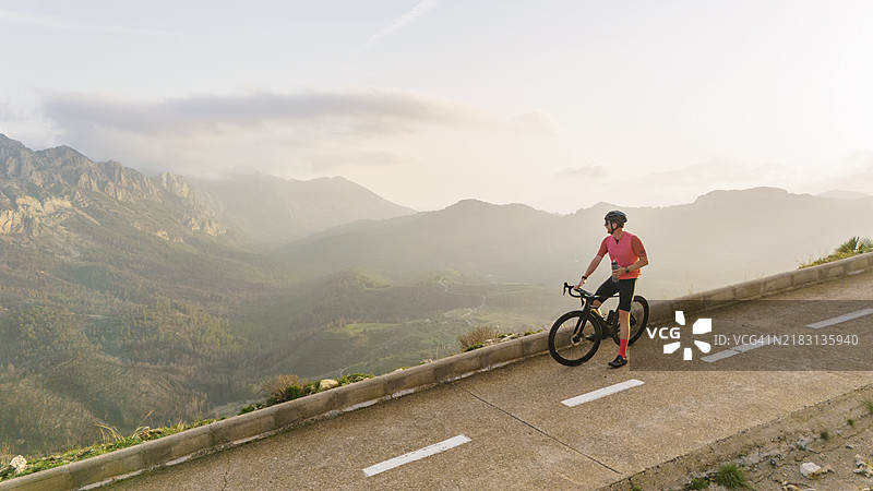 成熟的骑自行车者停下来，欣赏西班牙山区美丽的日落景色。图片素材