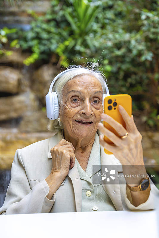 一位老年女性在养老院里用手机听音乐的竖版肖像。图片素材