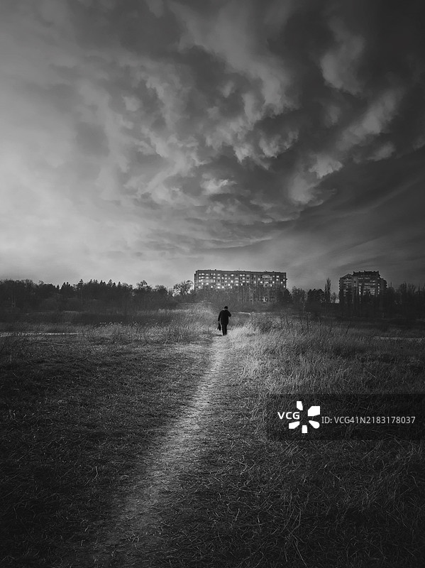 黑白场景，垂直拍摄的流浪者剪影走在狭窄的小径上穿越荒野。宁静的傍晚氛围，戏剧性的风景，孤独与独处的概念。图片素材