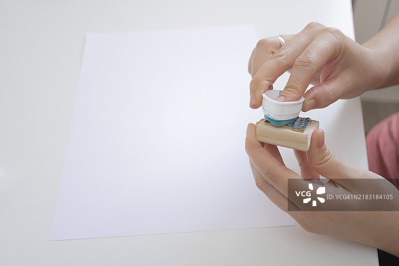 女人的手在背景中将橡皮图章浸入墨水，面前是一张空白的纸张准备盖章。图片素材