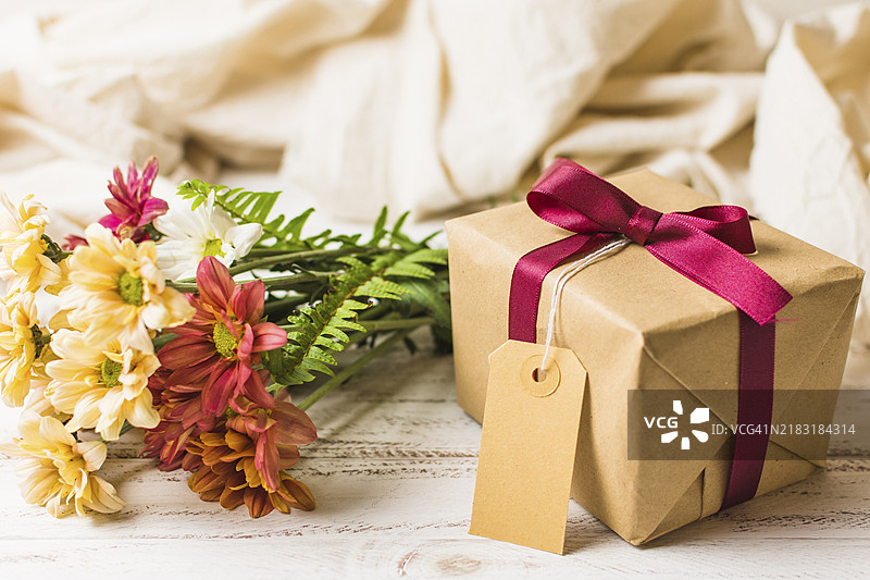 带有棕色标签的礼品盒与花束放在桌子上图片素材