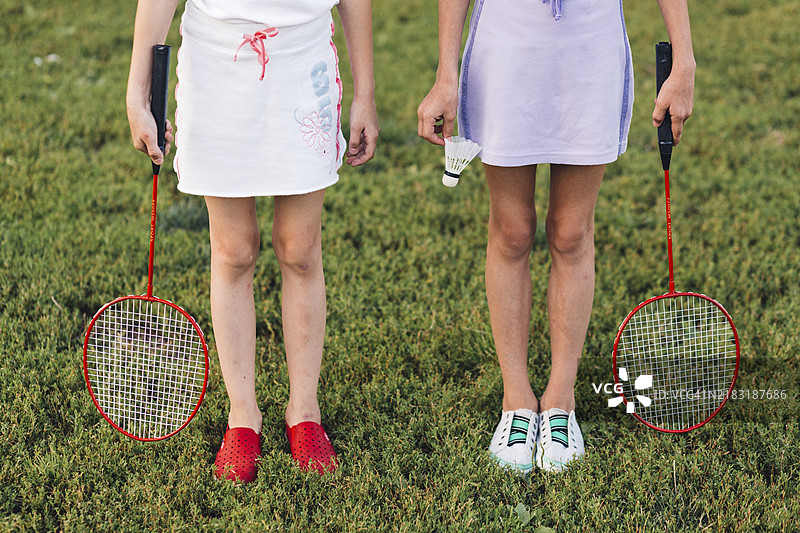 女孩站在绿草地上，手里拿着羽毛球。图片素材