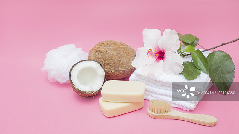 粉色背景上的肥皂刷、椰子海绵、花朵毛巾图片素材
