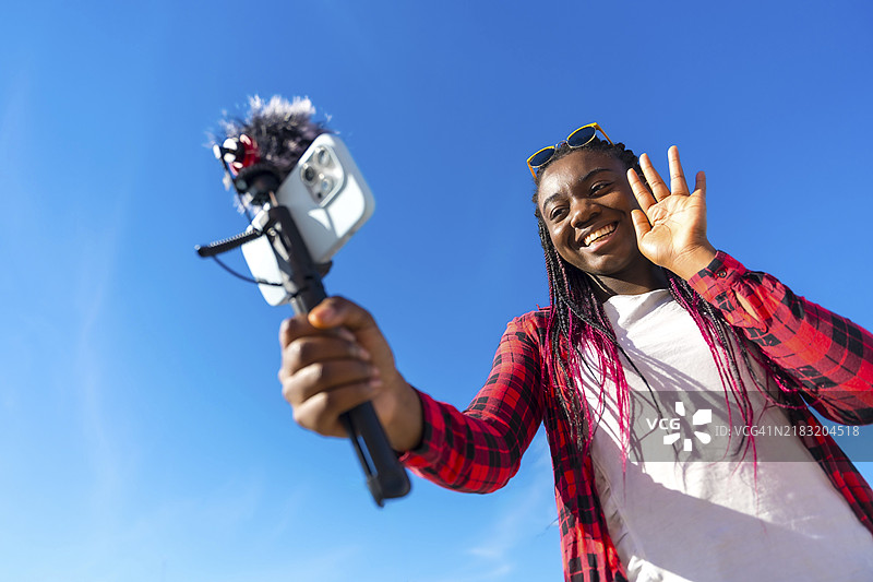 非洲女性在户外用手机和麦克风录制视频时挥手致意图片素材