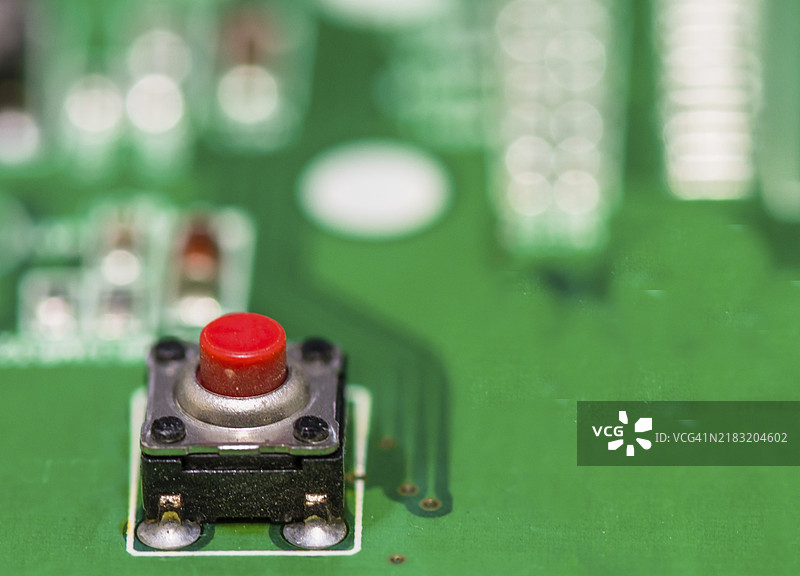 绿色电路板上的红色按钮，背景模糊的其他组件图片素材