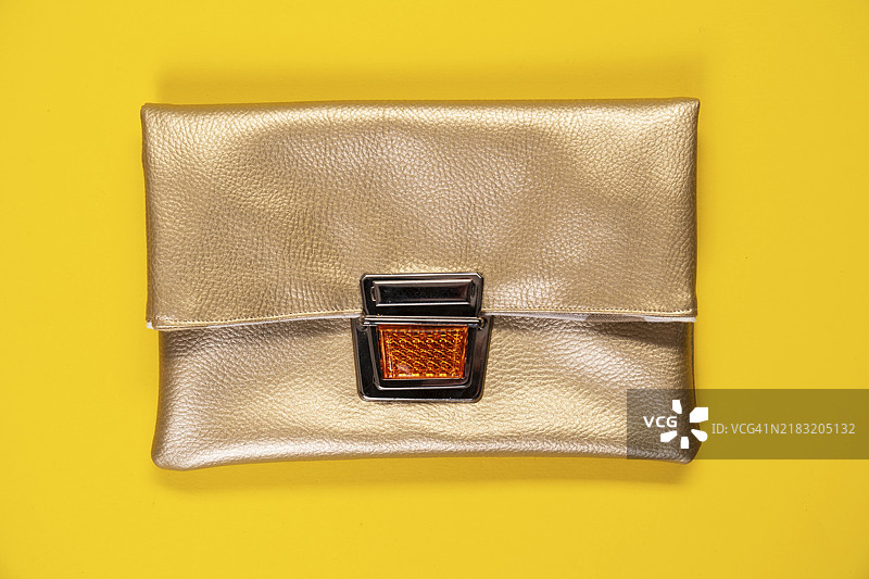 金色仿皮手拿包置于纯黄色背景上图片素材