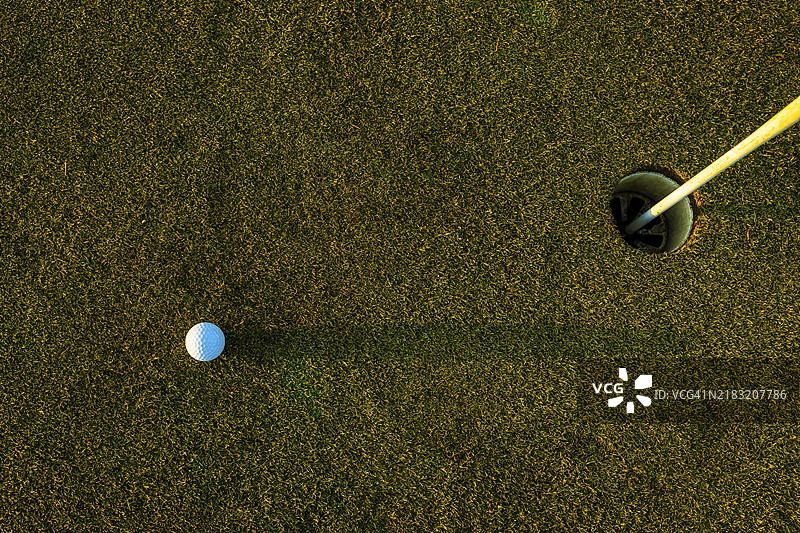 瑞士高尔夫球场日落时分的果岭上，草地上的高尔夫球、阴影和带旗杆的洞。图片素材