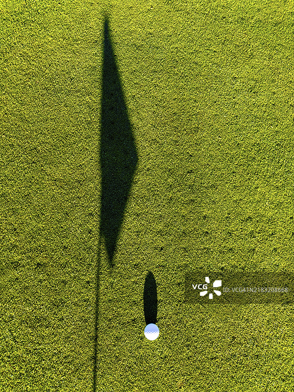 阳光明媚的瑞士，果岭上的高尔夫球和高尔夫旗的影子图片素材