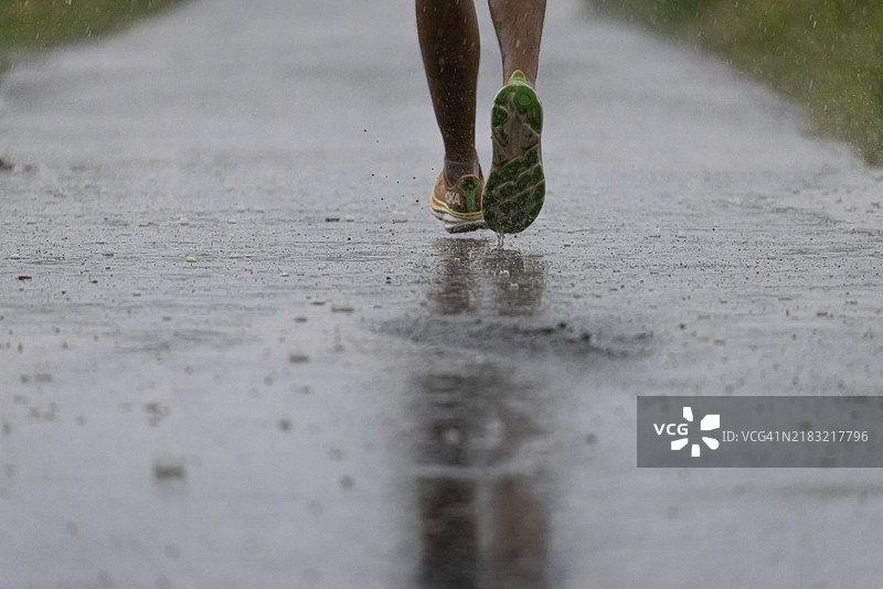 一名慢跑者在德国黑森州法兰克福市西北部的泥土小道上，在大雨中奔跑。图片素材