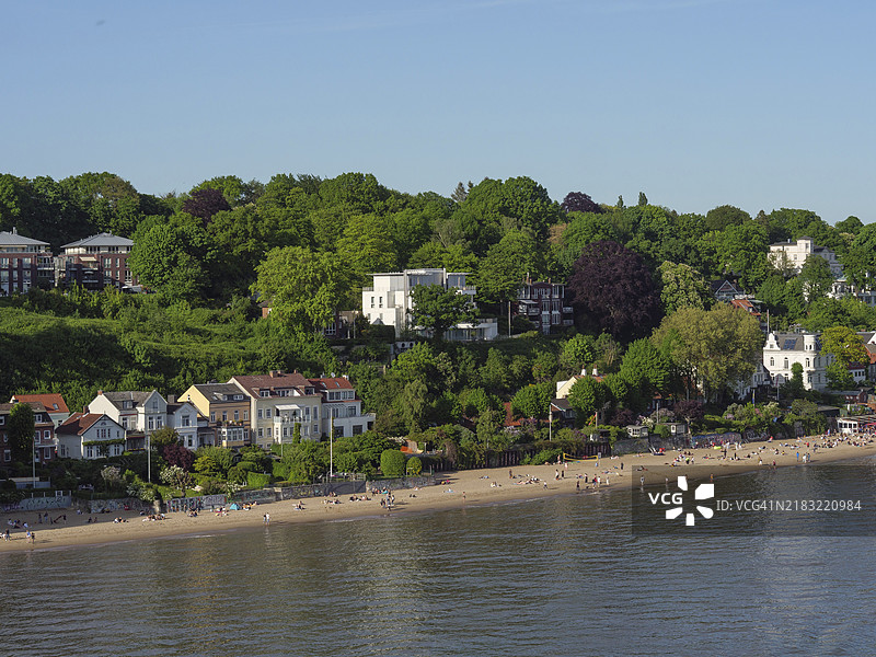 一个宁静的海滩，前面是一座郁郁葱葱的小山，山上有小房子，气氛悠闲，德国汉堡图片素材