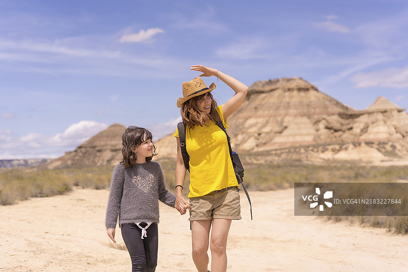 母亲和女孩手牵手在干旱的国家公园散步的水平正面视图图片素材