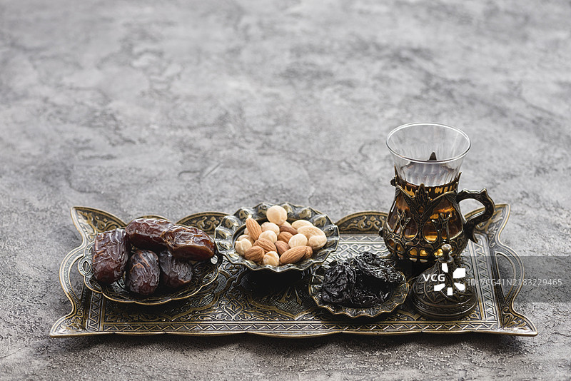 传统土耳其阿拉伯茶杯、日期坚果、金属托盘与混凝土背景图片素材