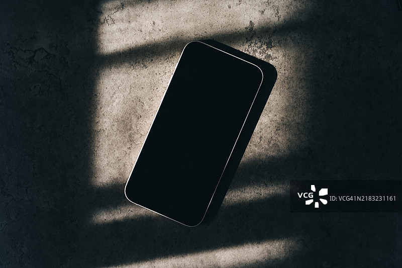 阳光明媚的日子里，桌子上放着一部黑屏的手机。图片素材