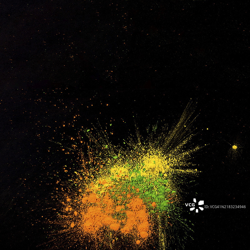 黄色、绿色和橙色的粉末在黑色背景上溅洒开来图片素材