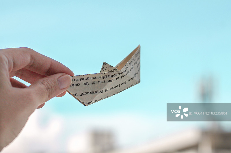 手握折纸船，背景是晴朗的蓝天图片素材