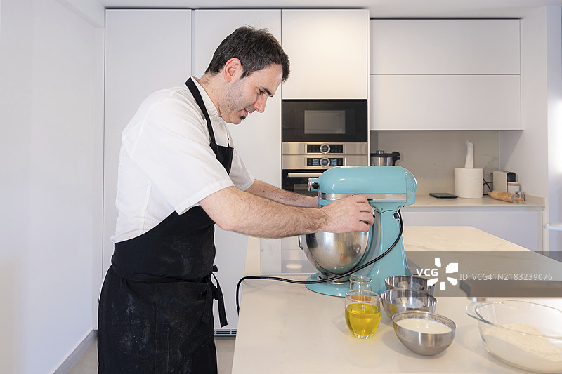 一名男烘焙师在家中制作红丝绒蛋糕，使用厨房机器人准备蛋糕，居家工作。图片素材