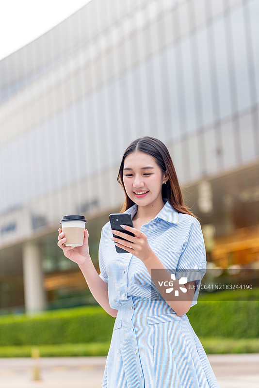 年轻亚洲女性在中央商务区户外使用手机并喝着咖啡图片素材