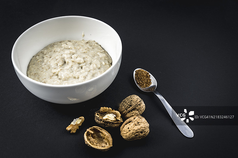 杯中的燕麦粥和带翅膀的核桃，糖和牛奶，背景为黑色。燕麦食谱包含核桃、梅干、肉桂和糖。图片素材
