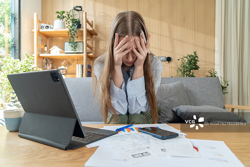 一位感到压力的女商人在家中使用笔记本电脑工作，神情忧虑、疲惫且不堪重负。图片素材