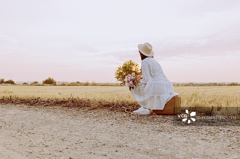 在麦田里，黄昏时分，一位西班牙裔女性坐在藤编野餐篮中。图片素材