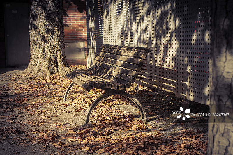 一张空荡荡的公园长椅被秋天的落叶环绕，投下阴影，散发着宁静，位于魏玛的街道上。图片素材