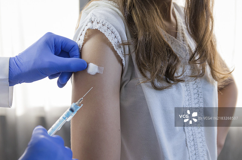 医生近距离握着注射器，使用棉球为戴着口罩的患者准备注射。新冠病毒疫苗。图片素材