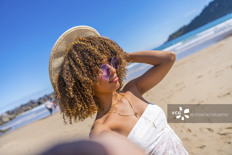一位佩戴太阳镜和帽子的拉丁美女在海滩上自拍的个人视角图片素材
