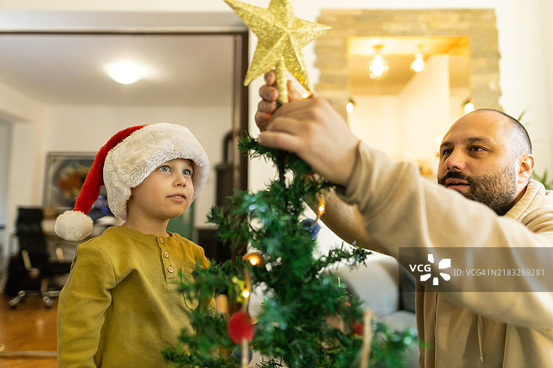 可爱的幼儿和父亲一起把星星放在圣诞树顶上图片素材