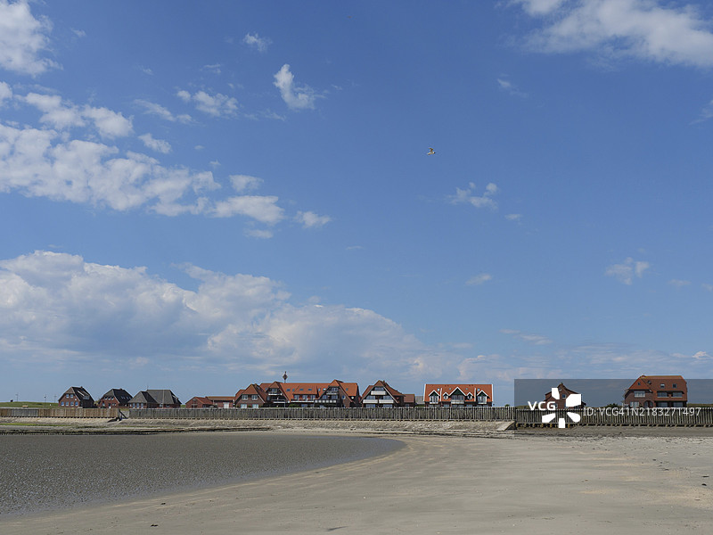 德国巴尔特鲁姆，一个红色房屋的定居点前的沙滩，蓝天白云。图片素材