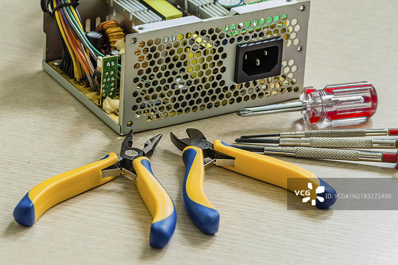 打开的台式机电源的侧视图，旁边有修理设备所需的钳子和螺丝刀。图片素材