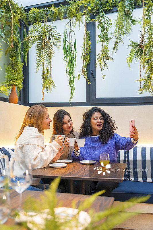 三位女性朋友在咖啡馆里喝咖啡时用手机自拍的竖拍照片图片素材