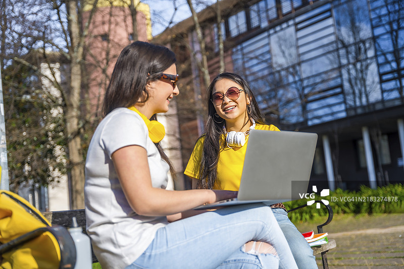 微笑的女性在校园外坐着用笔记本电脑学习图片素材