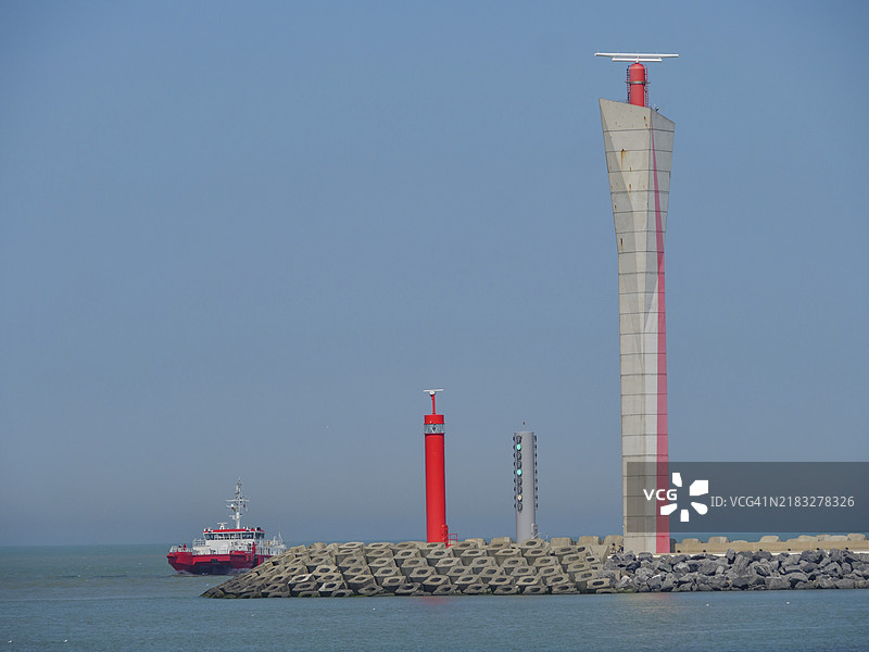 比利时海岸前的灯塔和一艘红色船只，背景是清澈的蓝天，灯塔位于海港入口，奥斯坦德，比利时，欧洲图片素材