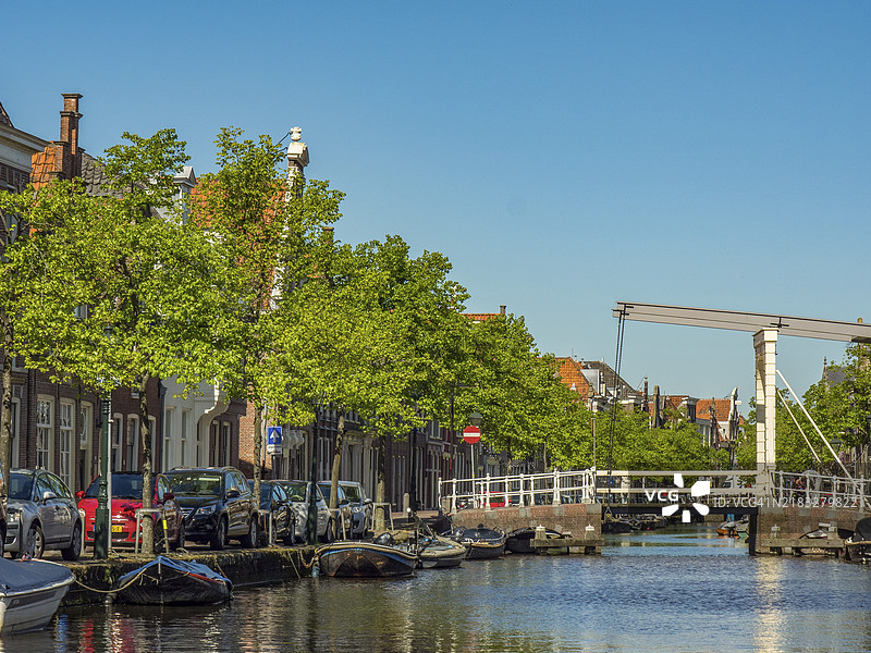 阿尔克马尔，荷兰的宁静运河风景，带有可升降桥，岸边停着汽车，蓝天下绿树成荫。图片素材
