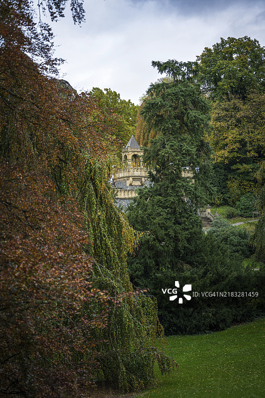 浓密的秋季树木遮挡了城堡般建筑的视野，建筑上有城垛，营造出宁静的氛围，地点为巴门的迪克·伊巴赫台阶，巴门公园，伍珀塔尔，北莱茵-威斯特法伦。图片素材