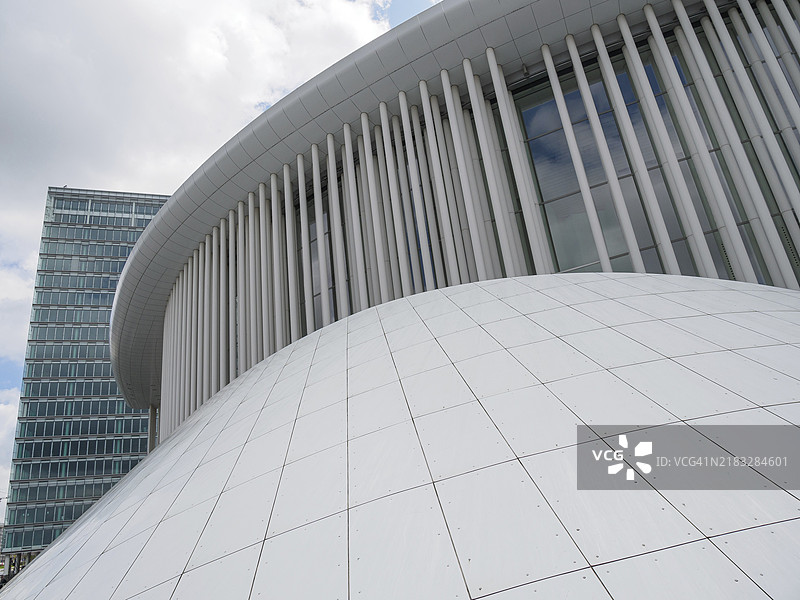 白色弯曲结构位于现代玻璃立面前，天空多云，现代建筑与树木和玻璃立面相结合，卢森堡图片素材
