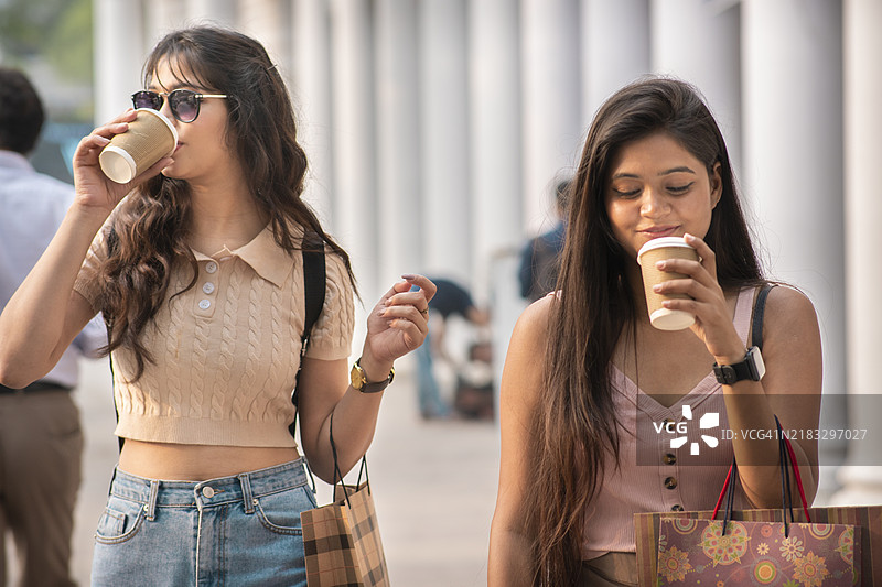 快乐的女性朋友们在城市街道上边走边享受外带咖啡图片素材