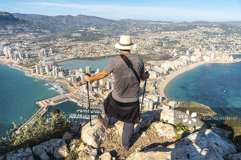 一位年轻的徒步旅行者站在西班牙瓦伦西亚自治区卡尔佩的伊法赫岩自然公园顶端，俯瞰地中海，欣赏坎塔尔罗伊格海滩和拉福萨海滩的美景。图片素材