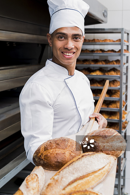 微笑的年轻男面包师展示刚出炉的面包和木铲图片素材