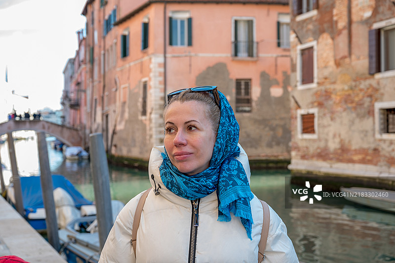 一位五十岁的金发游客在威尼斯，头上戴着蓝色围巾，面带甜美的微笑。图片素材