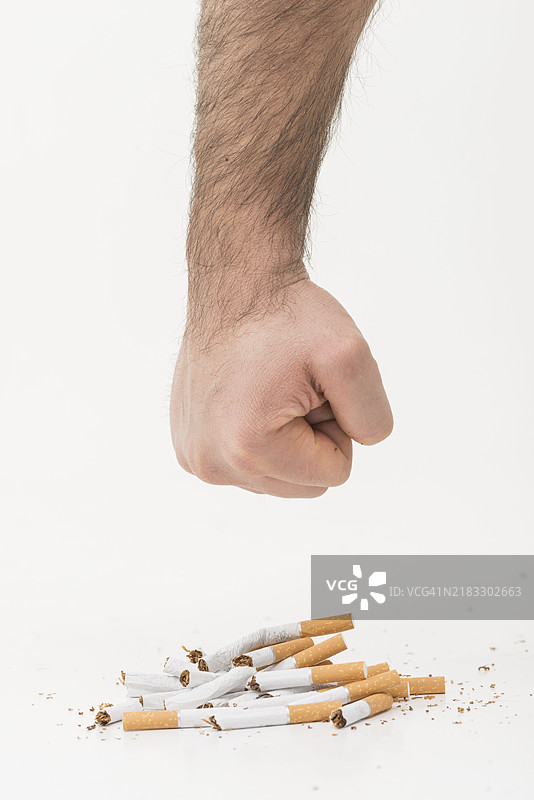 男人的手在白色背景上挥出拳头，旁边是断裂的香烟。图片素材