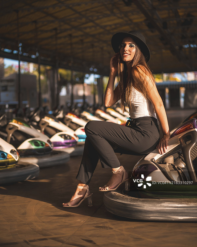 生活方式，棕发白人女性穿着长裤、白色T恤和黑色帽子，在游乐园的碰碰车上。图片素材