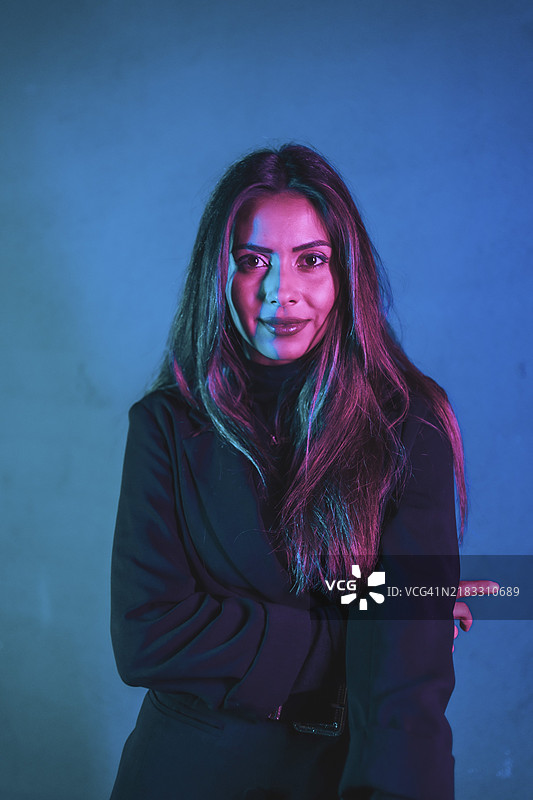 年轻的白人模特在蓝色和粉色霓虹灯的照射下，背景是蓝色墙壁。图片素材